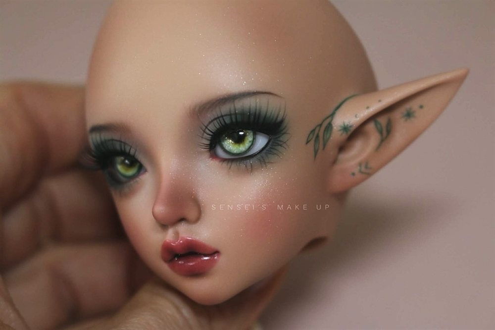 Elf doll face-up with green eyes, dark green lashes and tiny painted leaves on the pointed ear.
