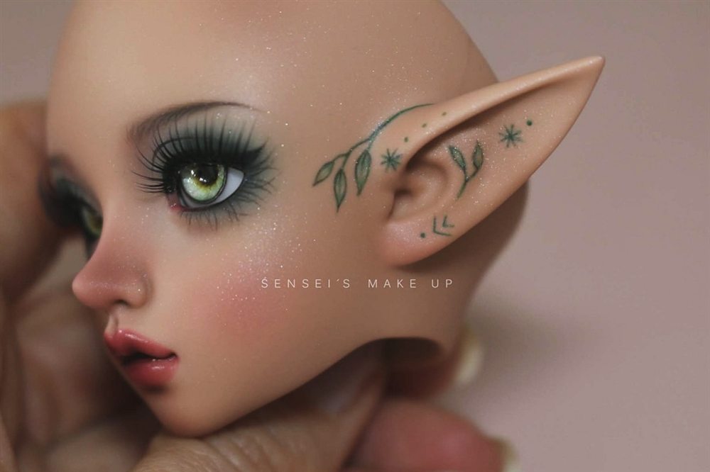 Side view of an elf doll with green eyes, smoky green lashes and tiny leaves and stars painted on the cheek and pointed ear.
