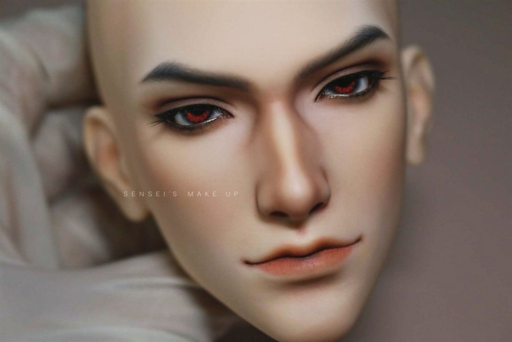 Male doll face-up with red eyes, strong dark brows and a soft coral lip.