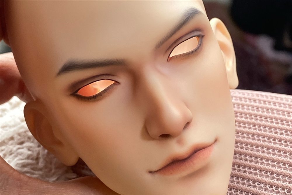 Male doll face-up with glowing amber eyes, dark sculpted brows and a soft natural lip.