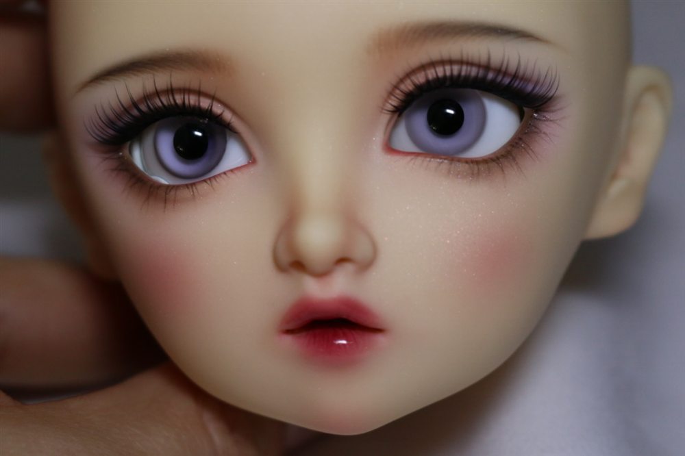 Close-up of a doll face-up with lilac eyes, fine lashes, a hint of glitter on the cheeks and a glossy red lip.