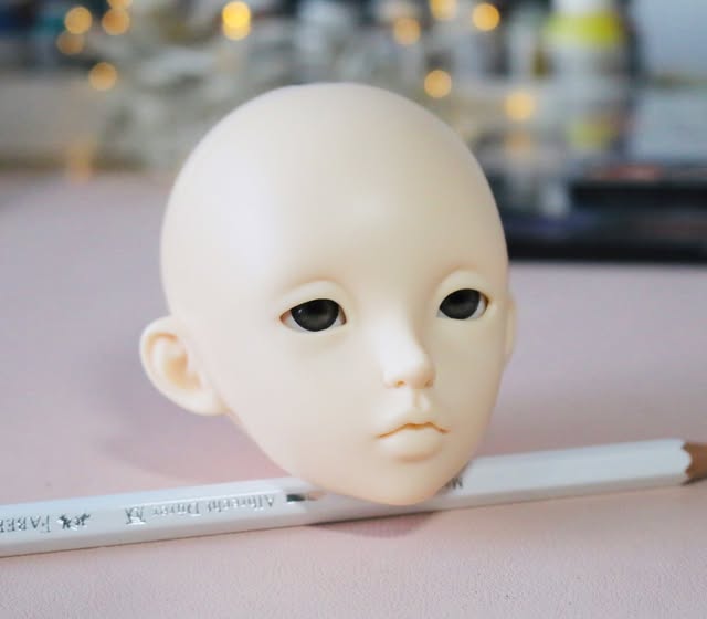 A blank resin doll head resting next to a white pencil, ready to be painted.