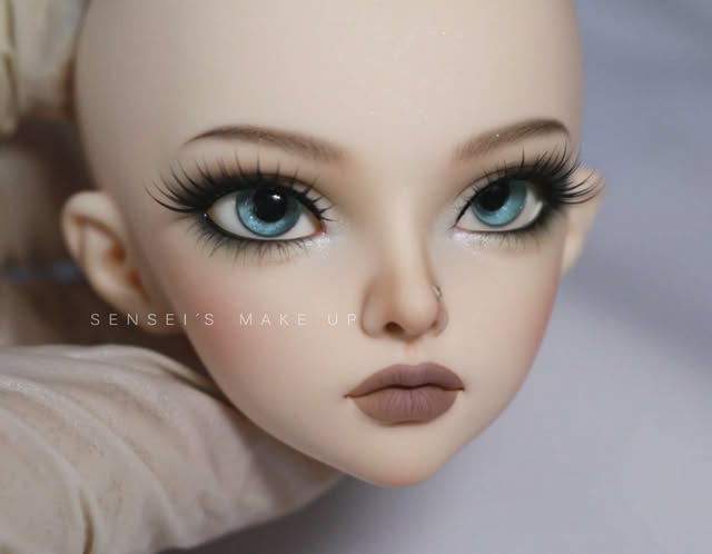 Close-up of a BJD face-up with blue eyes, thick lashes, soft blush and a mauve matte lip.