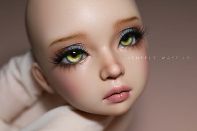 Doll face-up with yellow-green eyes, pale blue eyeshadow, peachy skin and a dusty pink lip.